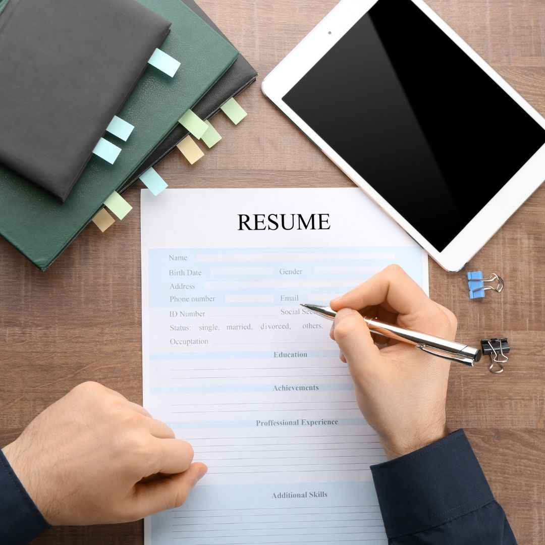 A resume on a desk with two notebooks and a tablet.